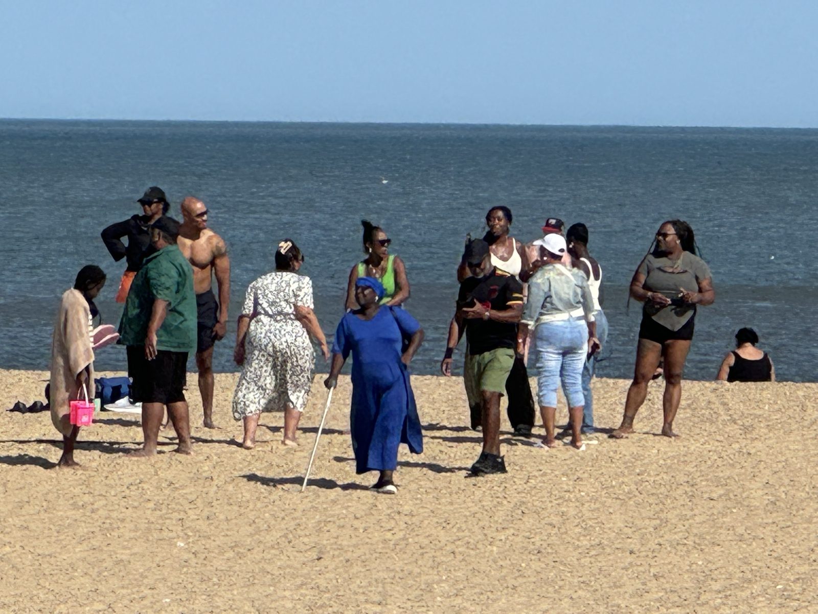 A group of people standing and chatting on a sandy beach by the sea