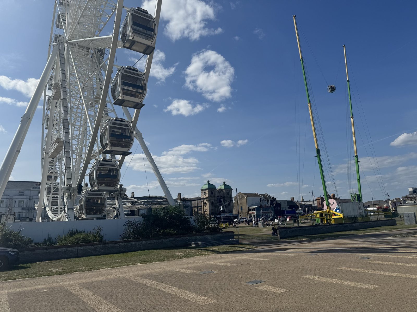 The observation wheel and a tall ride on the seafront under a blue sky