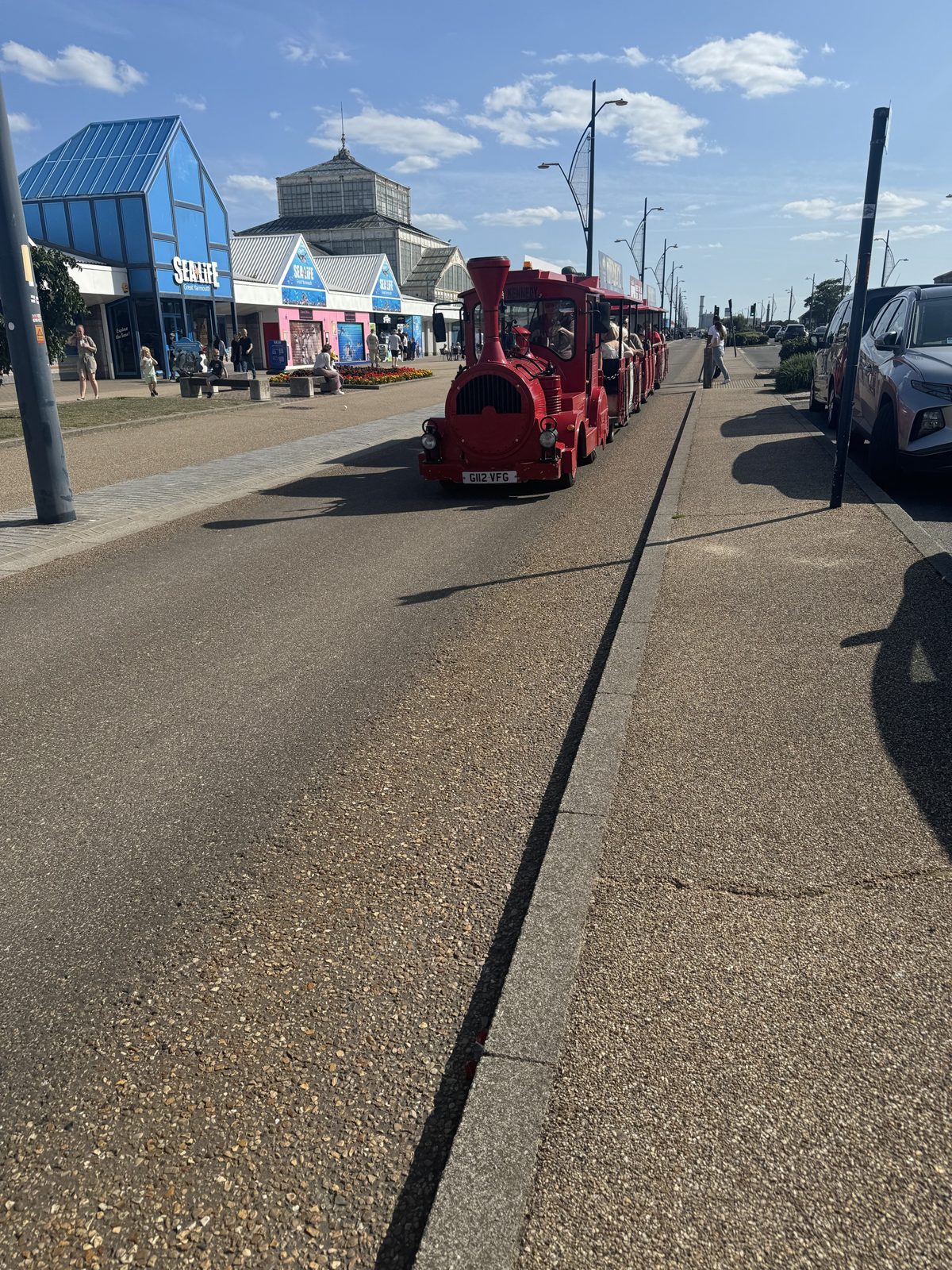 A red land train carrying passengers along the promenade